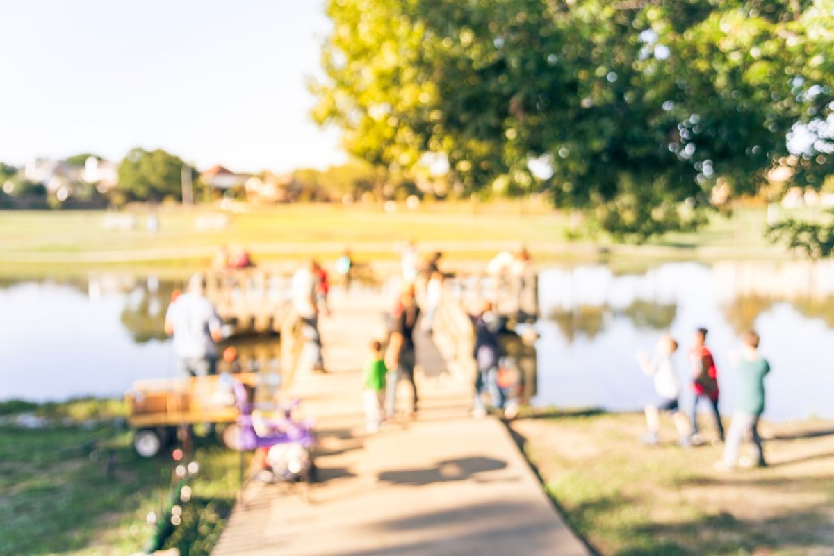 Vintage tone motion blurred family kids fishing near wooden pier/dock at lake pond. Free community event sponsored by neighborhood association. Defocused people fishing at the lakeside of urban park