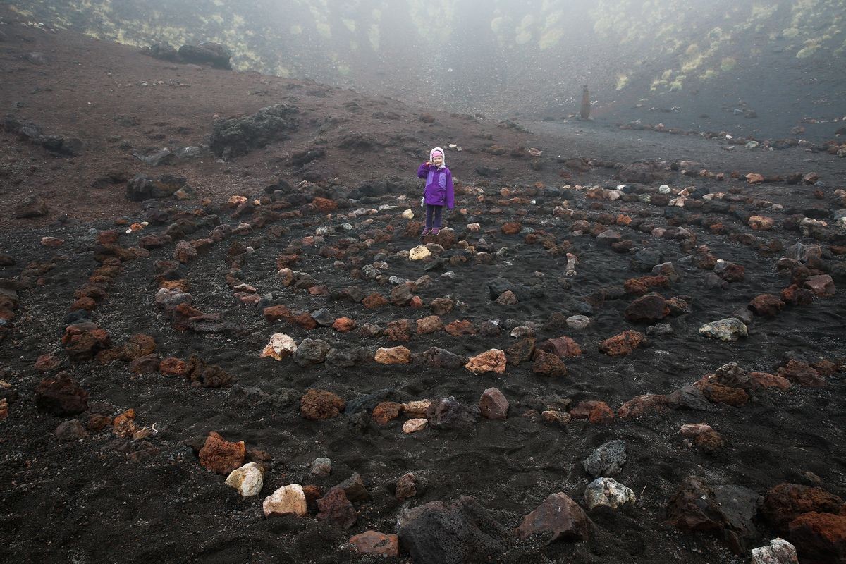 Child standing in center of a spiritual spiral of igneous rock in Etna volcano crater. Spiral symbolizes centering and widening consciousness. Spirituality, symbolism and psychic concepts. 